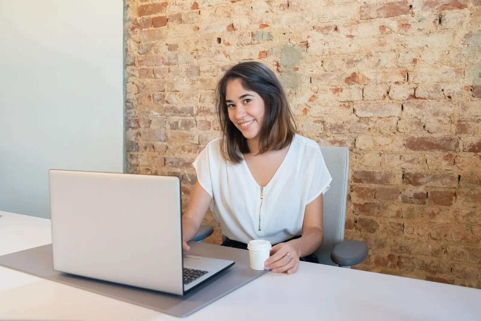 Mujer latina trabajando desde casa con laptop y café en su escritorio