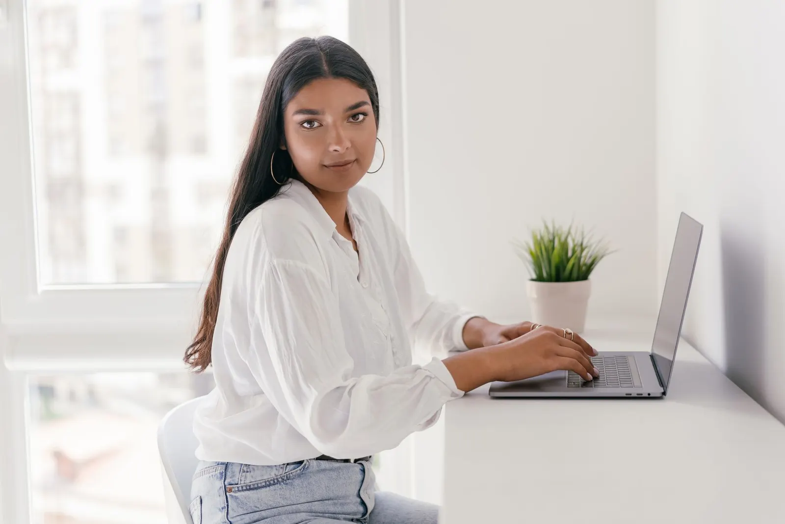 Mujer latina escribiendo en laptop en un escritorio luminoso de su casa